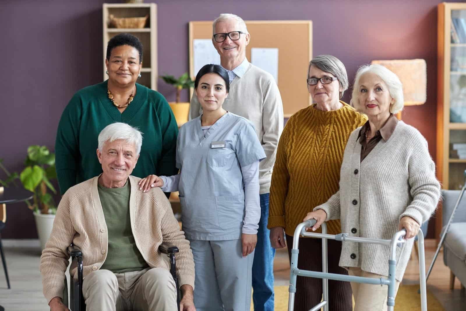Grupo de personas mayores y profesionales de cuidados posando juntos en una residencia, transmitiendo cercanía y diversidad.