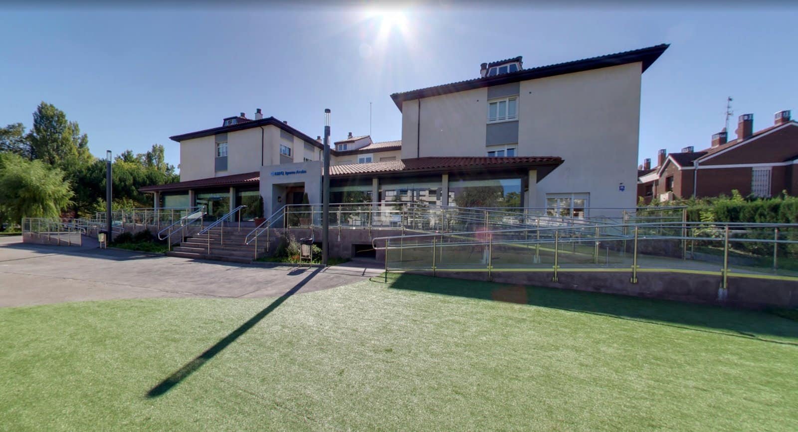 Entrada principal de la residencia para mayores IMQ Igurco Araba en Vitoria, con fachada moderna y accesible, rodeada de vegetación.