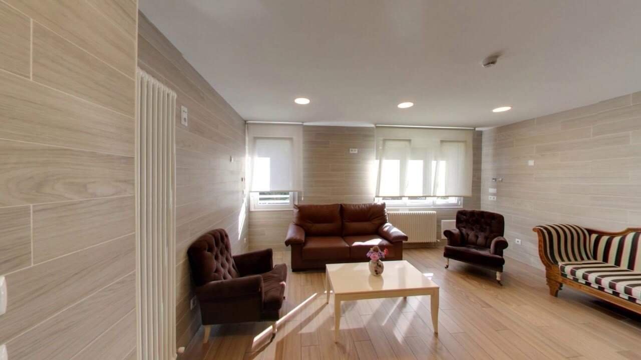 Sala de estar interior en la residencia IMQ Igurco Araba, equipada con sofás y sillones de estilo clásico, iluminación cálida y ambiente acogedor.