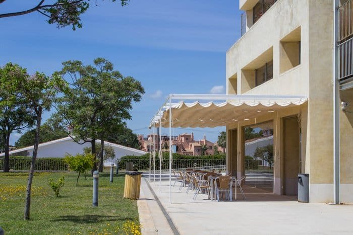 Terraza exterior de la residencia Vitalia Home Estepona, con zona de sombra, mesas y sillas para el disfrute al aire libre.