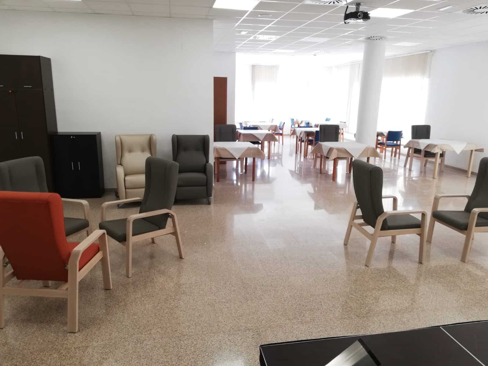 Una amplia y luminosa sala común de la residencia Colisée Alicante. Se observan varios grupos de sillas y sillones de colores, así como mesas preparadas al fondo, en un espacio diáfano con suelo brillante y grandes ventanales.