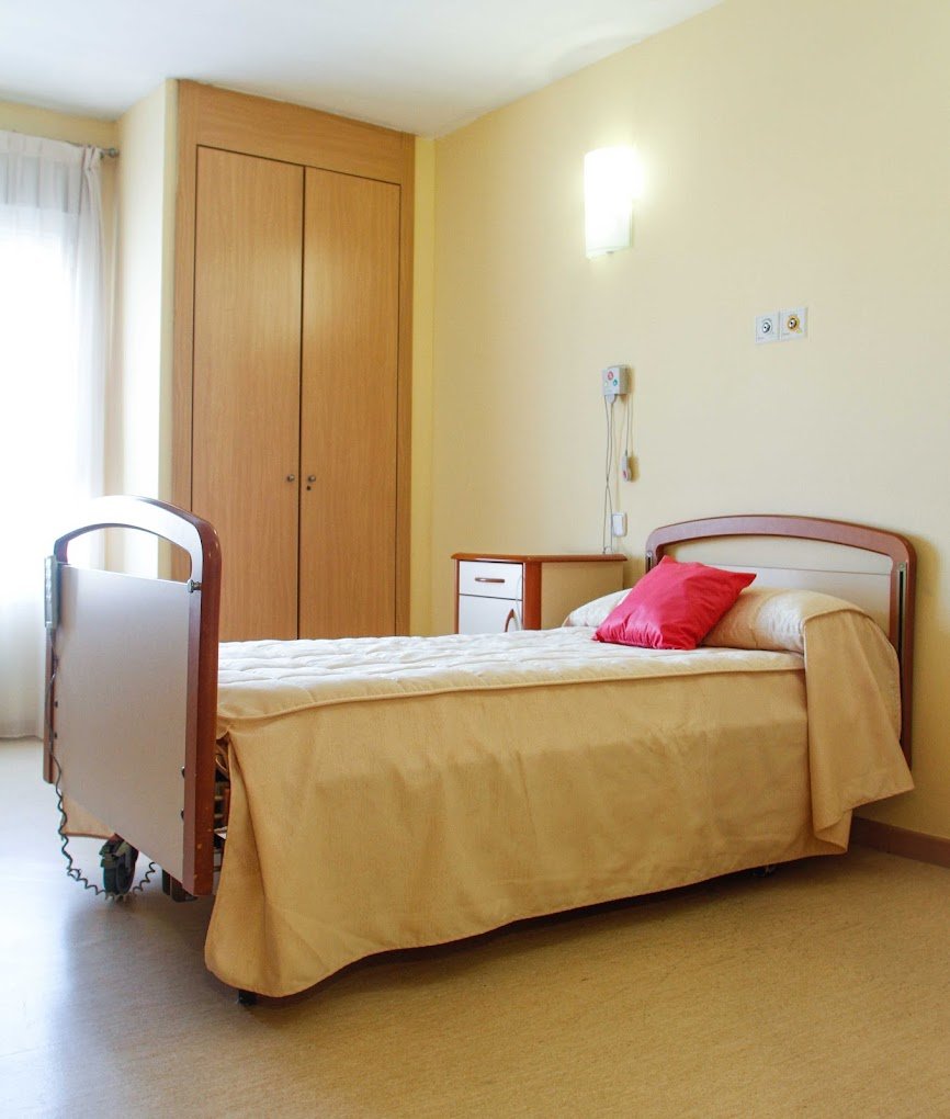 Un fisioterapeuta trabajando con un residente en silla de ruedas en la sala de rehabilitación, utilizando una máquina de pesas para fortalecer los brazos.