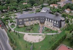 Fachada exterior del Pinar de Aravaca Centro Clínico Geriátrico, un edificio grande rodeado por un amplio jardín con árboles y un sendero pavimentado.
