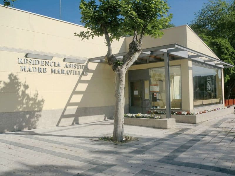 Fachada exterior del Centro Geriátrico Madre Maravillas, un edificio moderno con paneles de colores blanco y rojizo, y un gran letrero con su nombre.