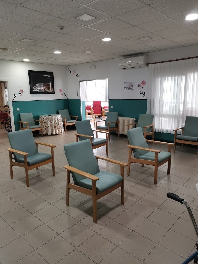 Sala de estar de la residencia, donde varios residentes y un miembro del personal conversan en un ambiente acogedor.