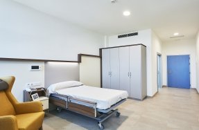 Residentes en sillas de ruedas y sillones participando en una actividad de grupo en la sala común de la residencia, con un miembro del personal al frente.