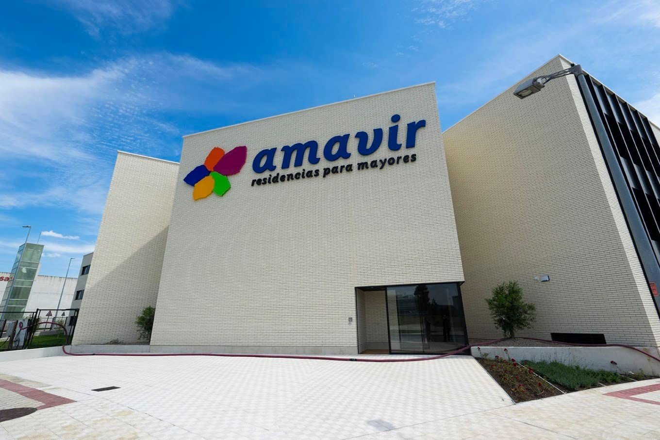 Fachada exterior de la Residencia Amavir Valle de Egüés, un edificio moderno rodeado por un jardín con césped y árboles.