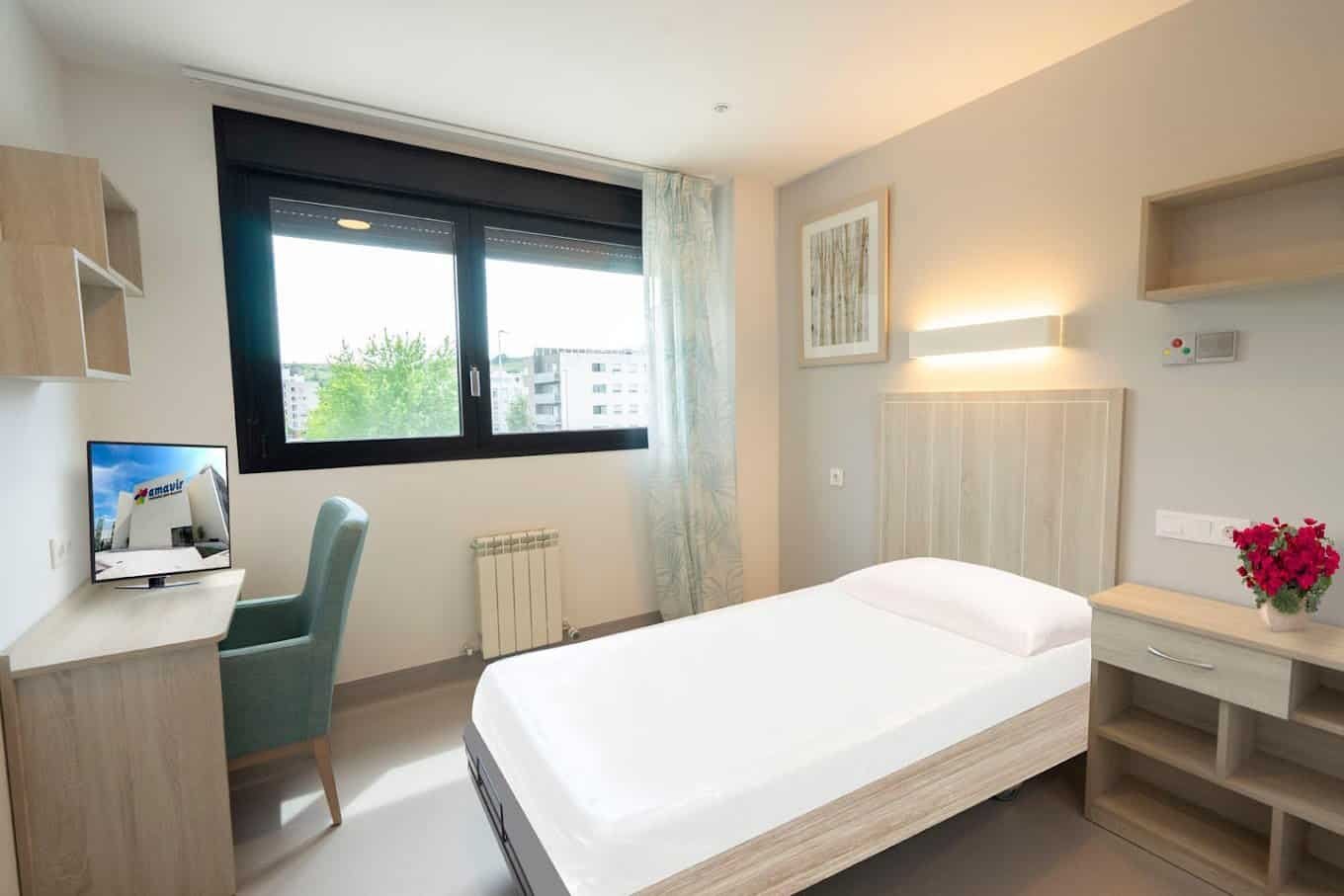 Sala de estar de la residencia con sillones y sofás en tonos neutros y azules, con una gran ventana que aporta luz natural.