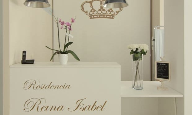 Recepción de la Residencia Reina Isabel, con un mostrador blanco, el nombre del centro en letras doradas y un logo de una corona en la pared.