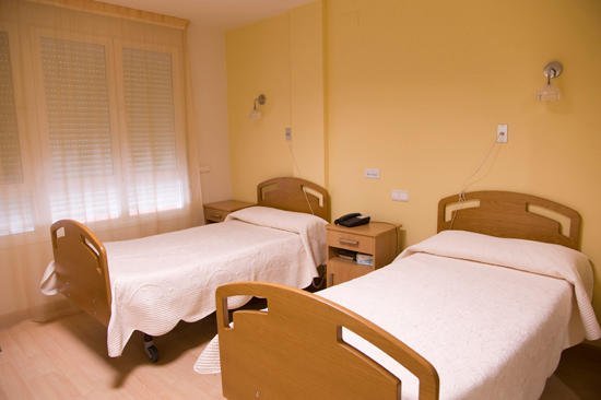 Habitación doble de la residencia con dos camas individuales, paredes de color amarillo claro y una mesita de noche con teléfono entre las camas.
