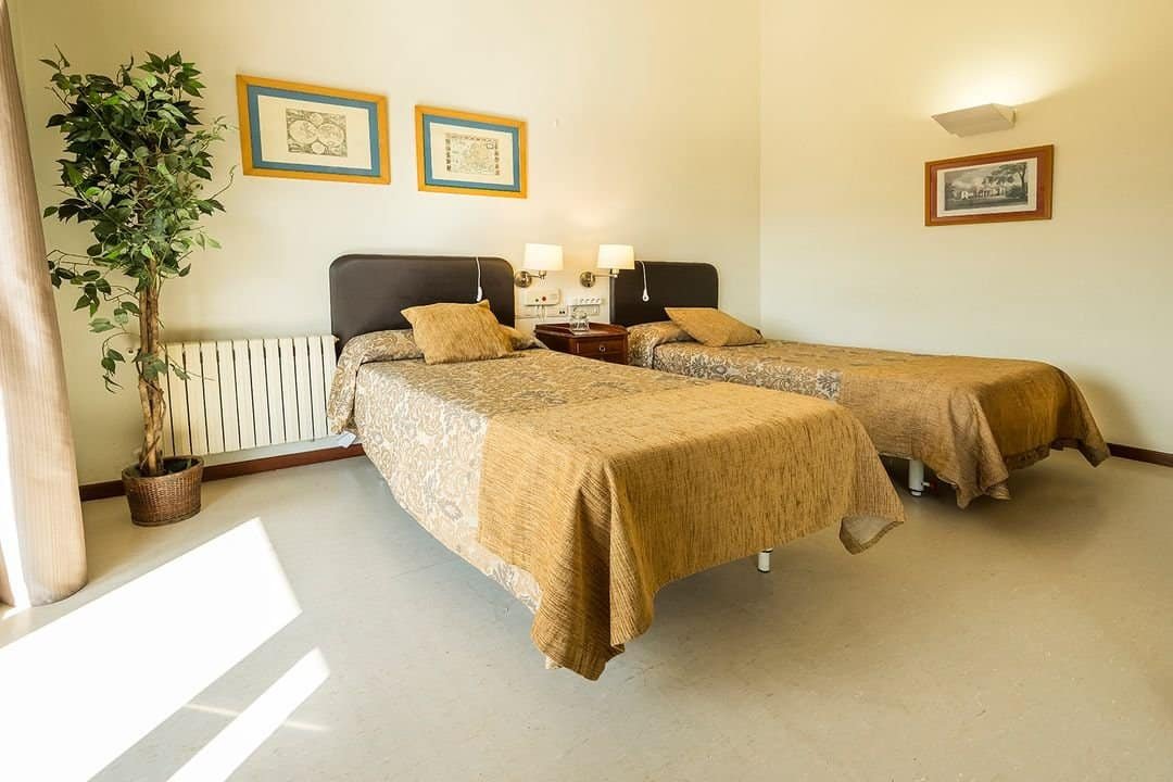 Habitación doble con dos camas, ropa de cama dorada y cuadros en la pared, con un ambiente cálido y luminoso.