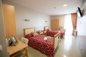 Habitación doble con dos camas, ropa de cama con patrones rojos y blancos, un escritorio y una ventana con cortinas rojas.