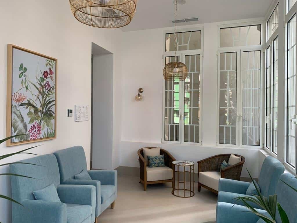 Sala común luminosa y moderna en la residencia, con sofás azules, sillones de mimbre y grandes ventanales.