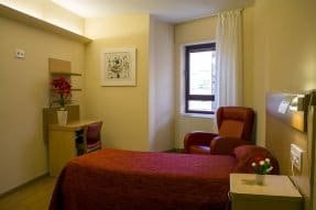 Habitación individual con una cama con edredón rojo, un sillón rojo y un escritorio, en un ambiente funcional y acogedor.