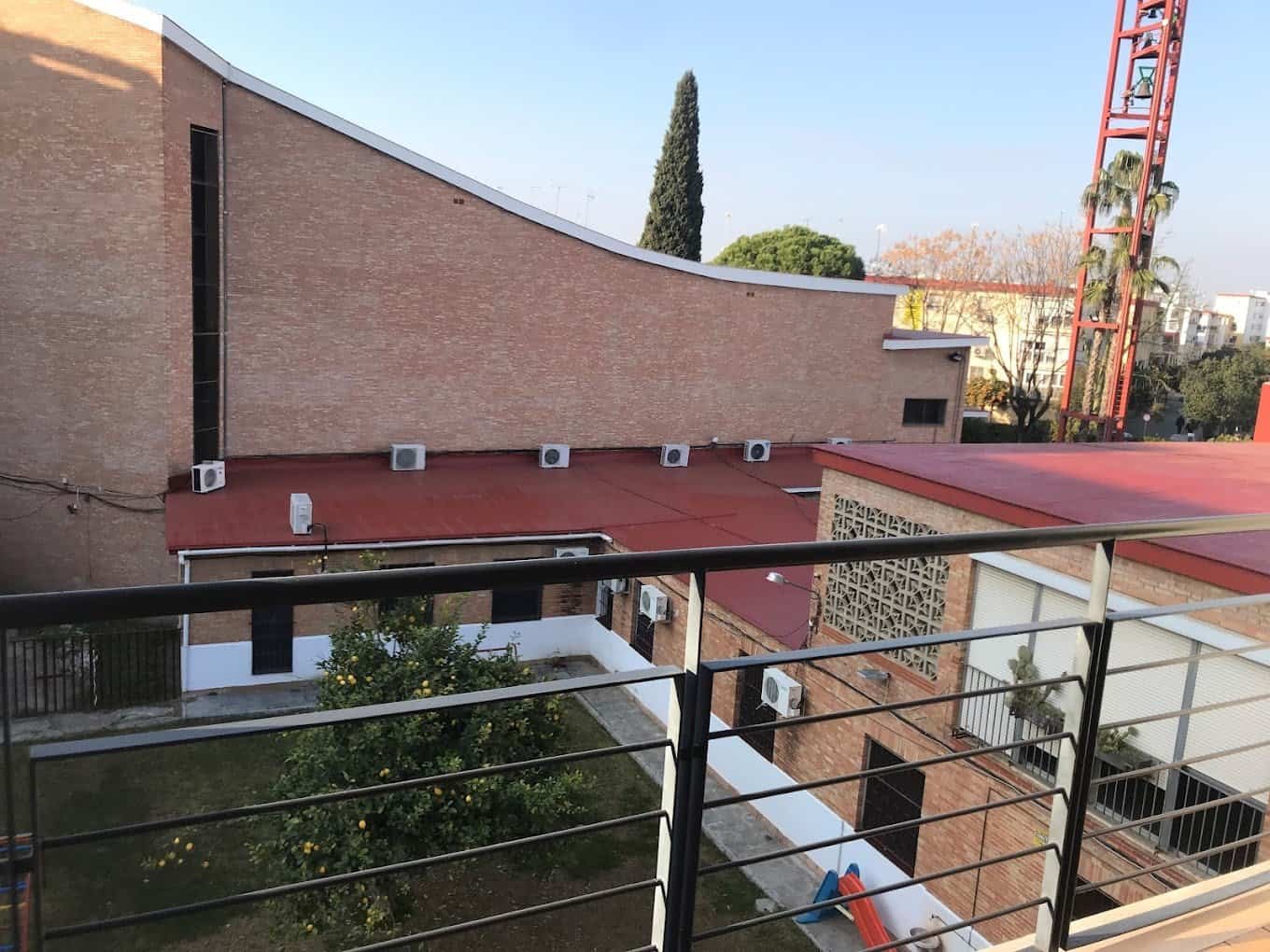 Vista desde un balcón de la Residencia San Eugenio Papa a un patio con un limonero, césped y un edificio de ladrillo al fondo.
