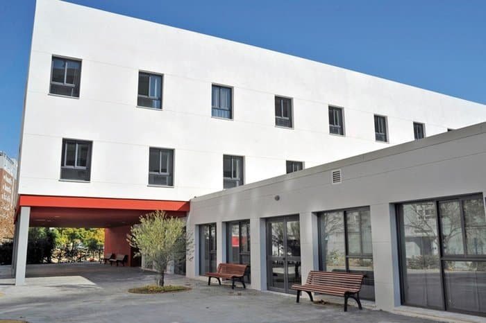 Edificio moderno de la residencia Vitalia Kansas con un patio interior, bancos, un árbol y un pasillo cubierto.