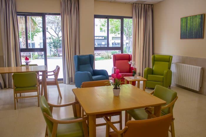 Sala común de la residencia Vitalia Kansas con sillones de colores vivos, mesas de madera y amplios ventanales.