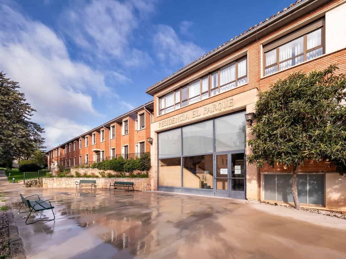 Edificio de ladrillo de la Residencia CleceVitam El Parque, con la entrada principal de cristal y un patio exterior con bancos.