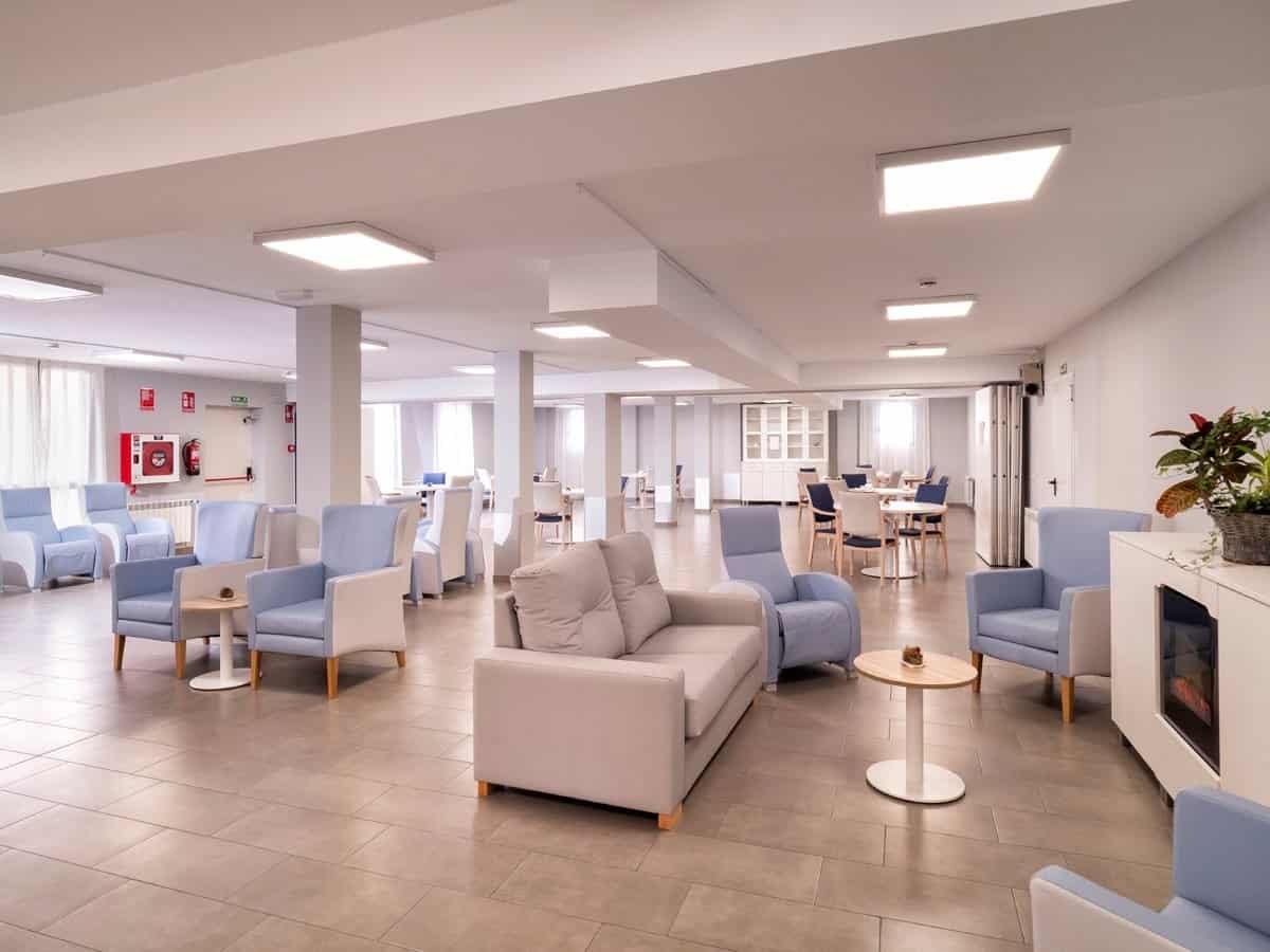 Sala común amplia y moderna en la residencia, con sillones grises y azules, sofás y mesas de centro.