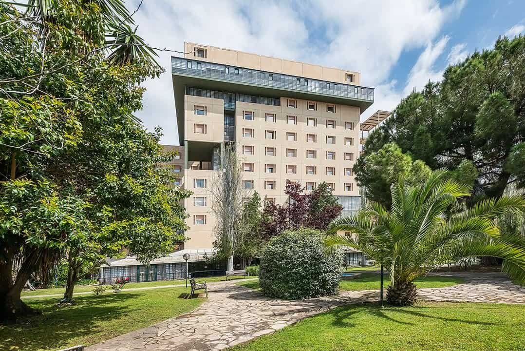 Edificio moderno de la Residencia Sanitas Tarragona, rodeado por un amplio jardín con césped, árboles y caminos de piedra.