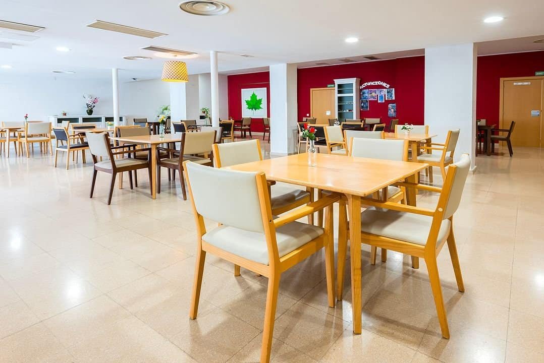 Comedor amplio y moderno de la residencia Sanitas con mesas y sillas de madera y paredes decoradas en rojo.