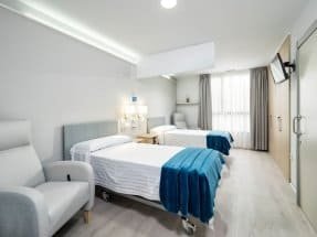 Habitación doble moderna y luminosa en la residencia CleceVitam Ponent, con dos camas y un sillón.