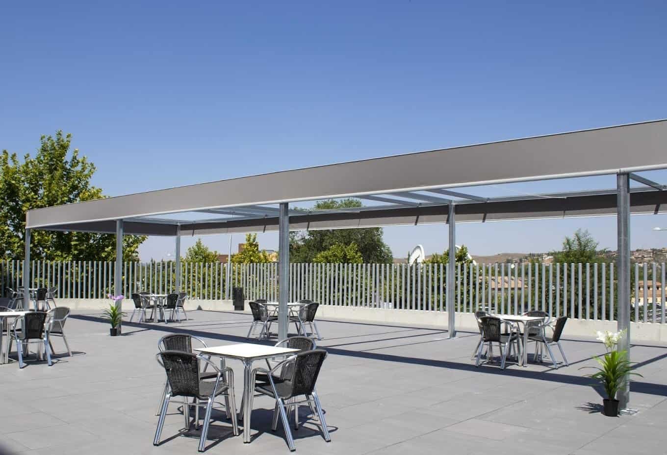 Terraza exterior en la azotea de Vitalia Home Toledo, con mesas y sillas bajo un toldo, y vistas de la ciudad en un día soleado.