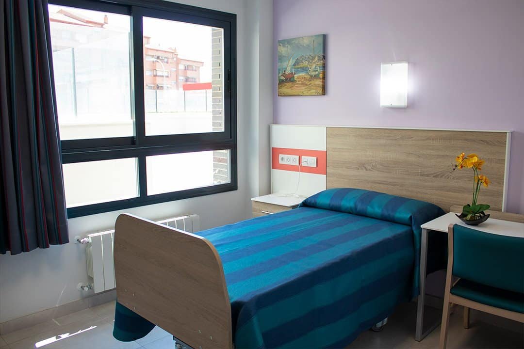 Habitación individual en Vitalia Home con cama, mesita de noche, silla y ventana, en un ambiente luminoso y moderno.
