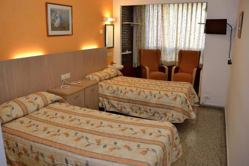 Habitación doble con paredes de color naranja, dos camas individuales, un lavabo y dos sillones junto a la ventana.