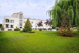 Edificio blanco de la Residencia de Mayores Sanitas, con un amplio jardín de césped, arbustos y un gran sauce llorón a la derecha.