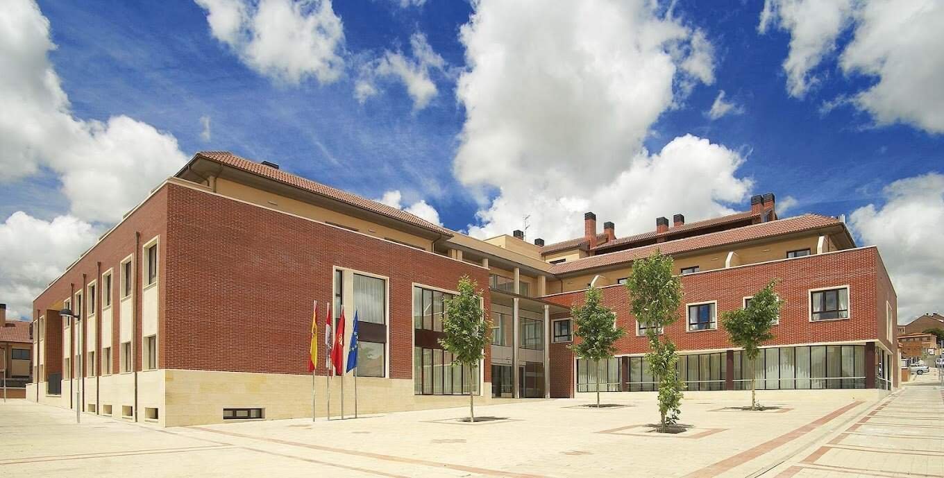 Edificio moderno de ladrillo de la residencia Colisée Plaza Real Valladolid, con un patio interior con árboles y pavimento bajo un cielo azul.