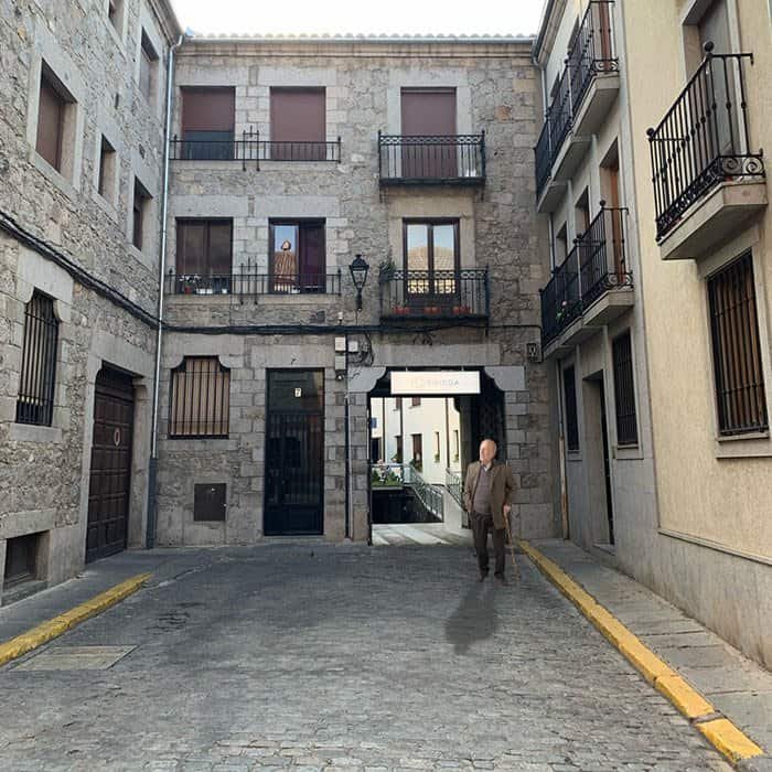 Un hombre mayor con bastón caminando por una calle empedrada entre edificios de piedra en un entorno histórico.