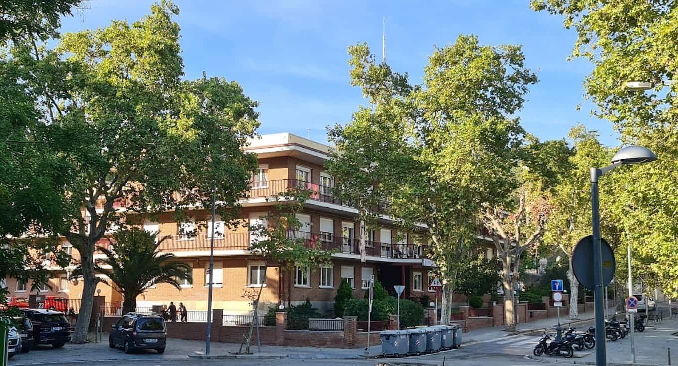 Edificio de ladrillo de varios pisos, presumiblemente una residencia, rodeado de árboles frondosos en un entorno urbano.