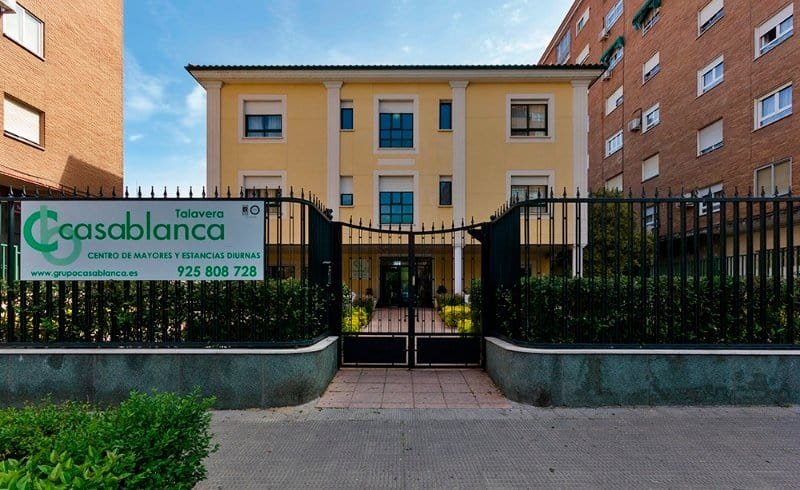 Vista exterior de un edificio de varios pisos con una fachada curvada de color gris, rodeado de palmeras y zonas verdes, en un entorno urbano.