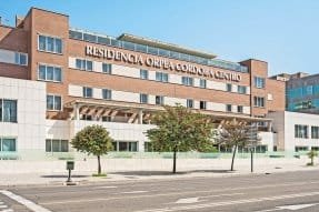 Vista exterior de la "Residencia Albatros", un edificio moderno de varios pisos con grandes ventanales y terrazas. La fachada es de color gris claro y el edificio está rodeado por un entorno de árboles y zonas verdes.