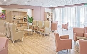Sala de estar luminosa con sillones altos, estantería decorativa y suelo de madera en la residencia Bouco Córdoba Centro.