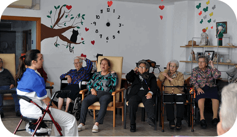 Grupo de personas mayores participando en una actividad dirigida por una profesional en sala decorada.