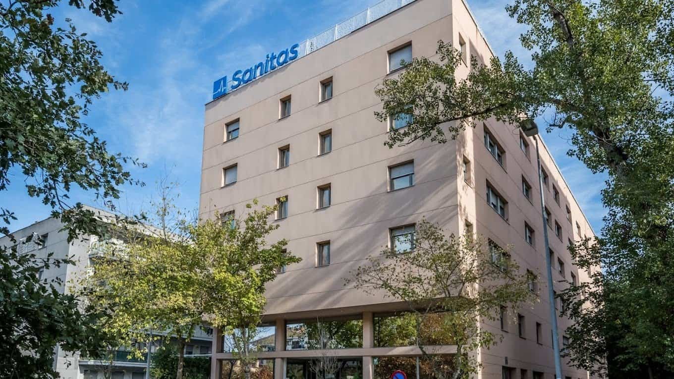 Edificio de la residencia de ancianos Sanitas en Madrid, con árboles y cielo azul.