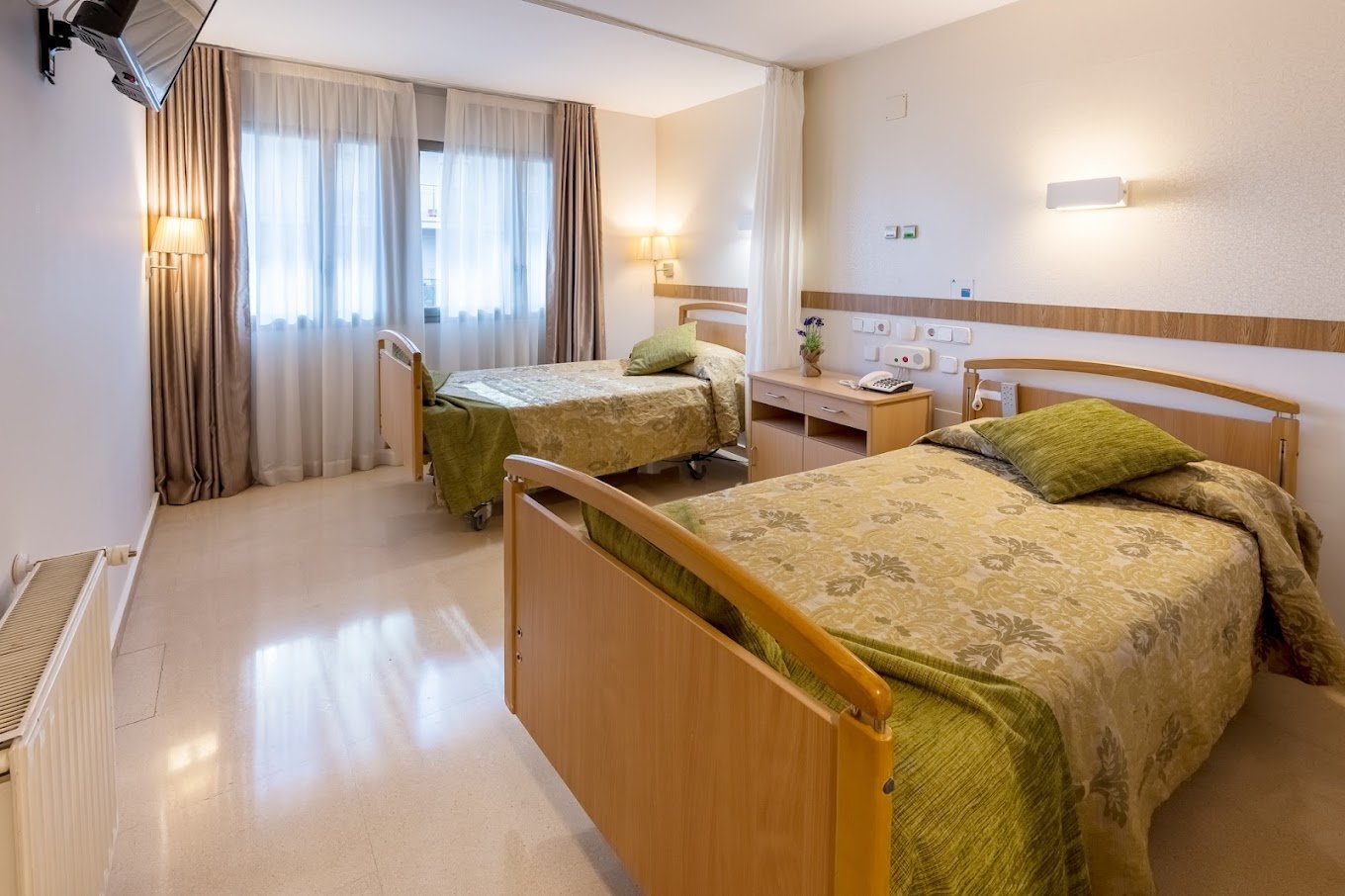 Habitación doble luminosa y limpia en la residencia de ancianos Sanitas, con dos camas individuales y mobiliario moderno.