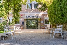 Fachada de la residencia ORPEA El edificio de ladrillo tiene un jardín con sillas blancas y árboles.