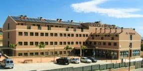 Edificio de una residencia de mayores de varias plantas, con paneles solares en el tejado, un aparcamiento exterior y un cielo azul.