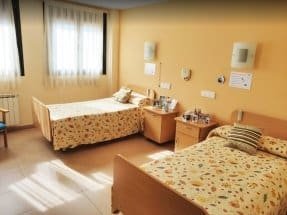 Habitación doble con paredes de color salmón, dos camas individuales con ropa de cama estampada y luz natural que entra por la ventana.