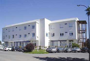 Edificio de un hospital o residencia de color blanco, con un aparcamiento delante.