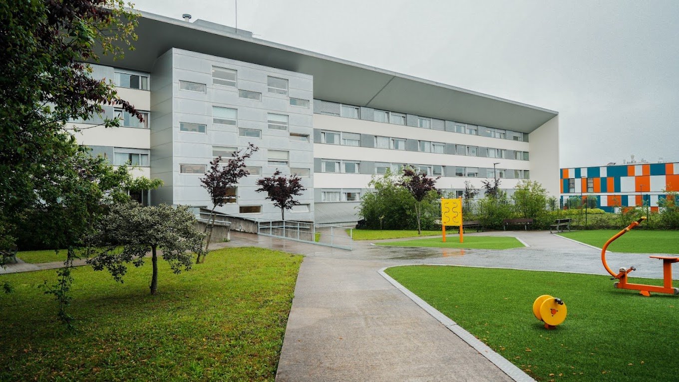 Edificio de estilo moderno con un techo inclinado, rodeado de césped y un pequeño parque con equipamiento de ejercicio exterior.
