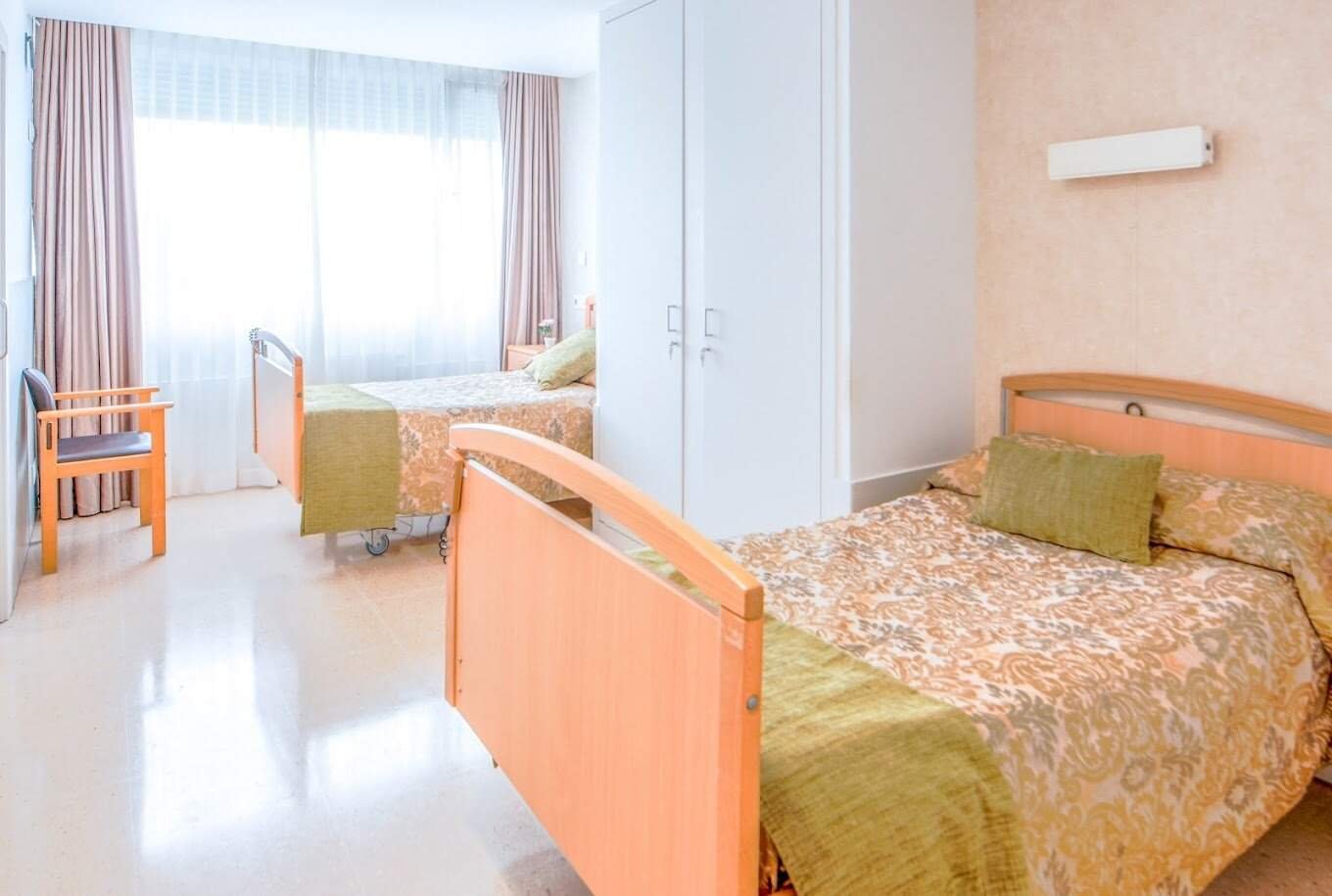 Habitación doble con dos camas individuales, un armario blanco y un gran ventanal con cortinas claras.