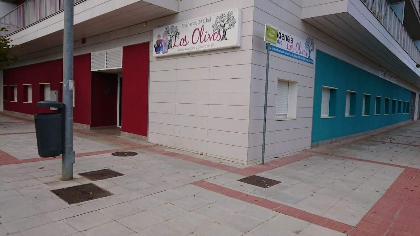 Esquina de un edificio con paredes de color blanco, rojo y turquesa. Hay un letrero con el nombre "Residencia Los Olivos.