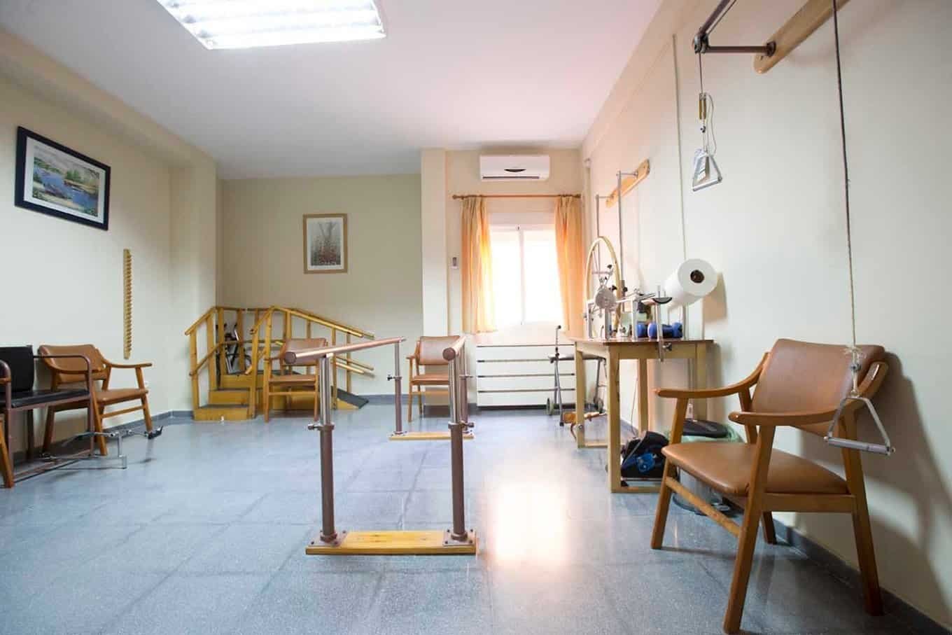 Sala de rehabilitación o fisioterapia con equipamiento como barras paralelas, escaleras y diferentes máquinas.