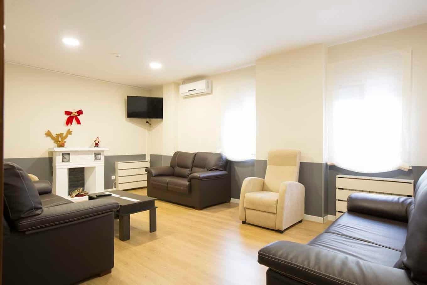 Sala de estar o de televisión con sofás de cuero de color oscuro y un sillón reclinable beige.