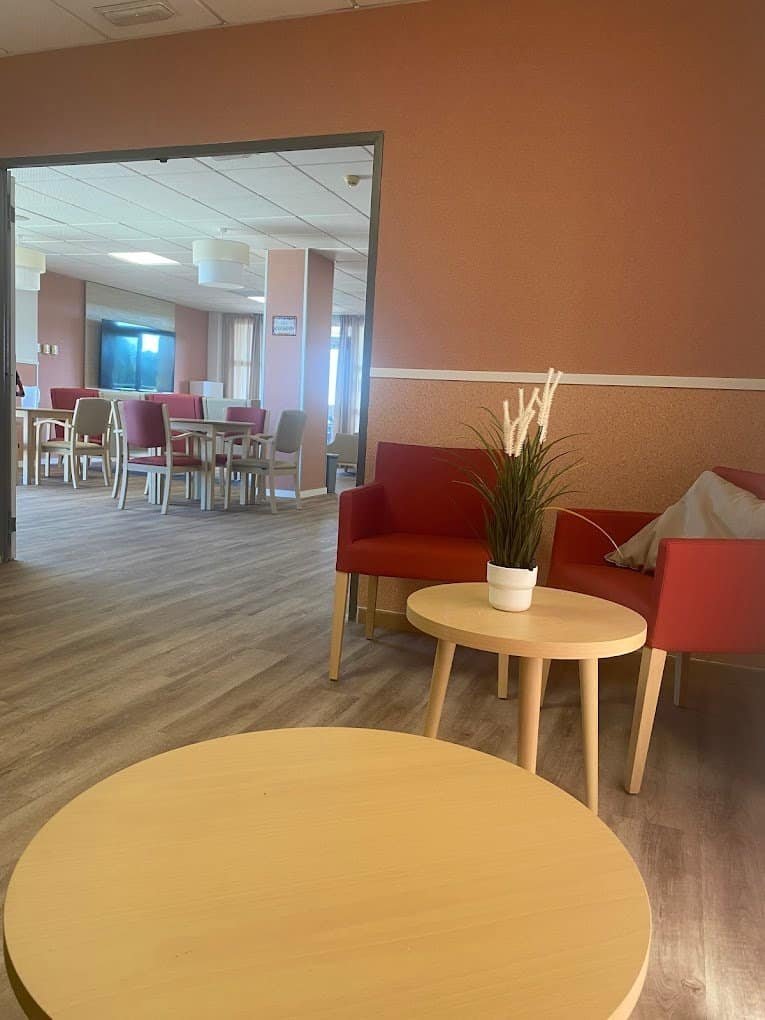 Zona de estar con sillas rojas y una mesa baja, que da a un comedor con mesas y sillas de color claro.
