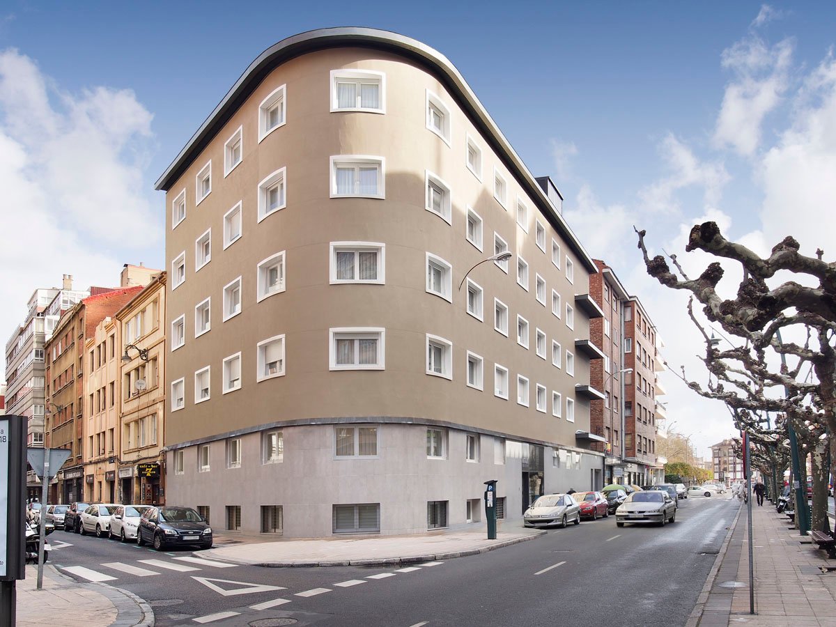 Fachada de un edificio curvo de varias plantas en una calle de la ciudad con árboles en la acera.
